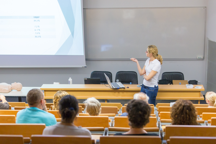Iliustracija, kurioje užfiksuota auditorija, lektorė ir studentai paskaitoje