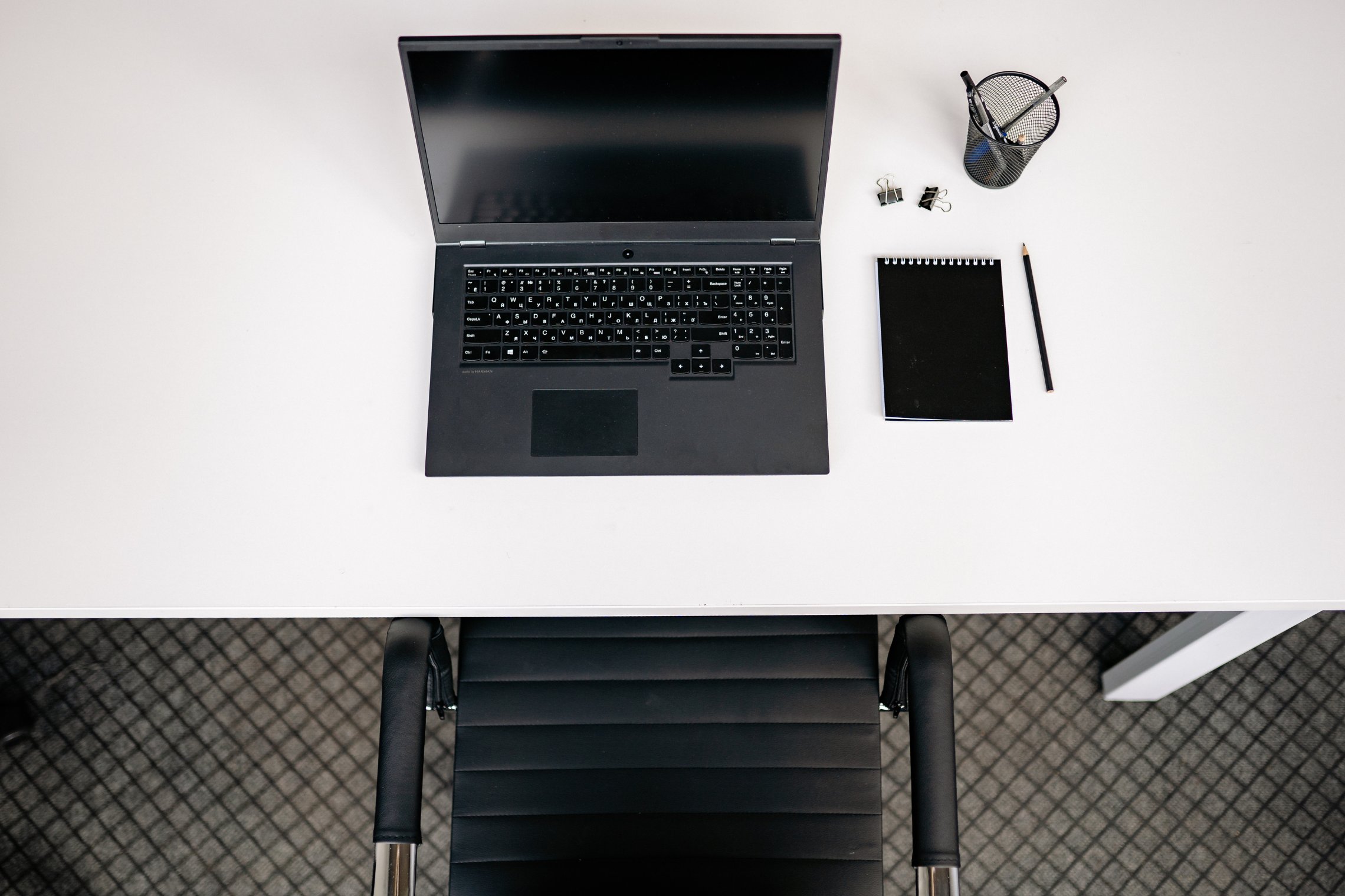 LT: Baltas darbo stalas iš viršaus su nešiojamuoju kompiuteriu, užrašine ir raštinės reikmenimis. / EN: Top view of a white desk with a laptop, notepad, and office supplies.