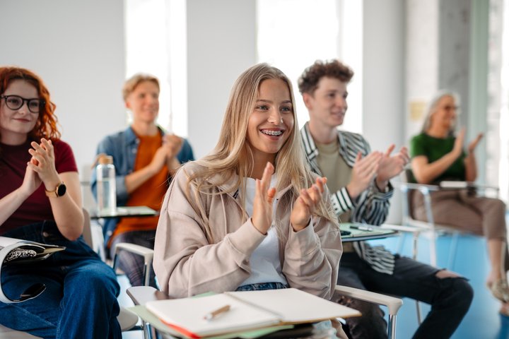 Lietuviškai: Prie stalų sėdi studentai ir klauso paskaitą. / English: Students are attending a lecture.